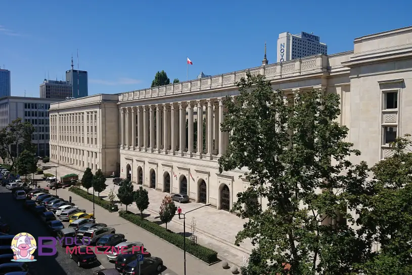 Gmach Ministerstwa Rolnictwa i Rozwoju Wsi w Warszawie, klasycystyczny budynek z kolumnadą, widoczny w słoneczny dzień, otoczony samochodami i zielenią.